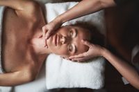 Kundin liegt entspannt auf der Behandlungsliege, während die Kosmetikerin im Beauty Room eine Gesichtsbehandlung durchführt