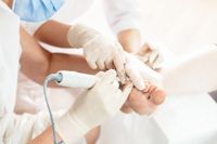 Kosmetische Fußpflege mit dem Fräser — professionelle Pediküre-Behandlung mit Handschuhen und Hygienemaske.