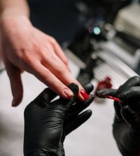 Detaillierte Aufnahme einer Hand während einer Maniküre mit rotem Nagellack, durchgeführt von einem Fachmann.